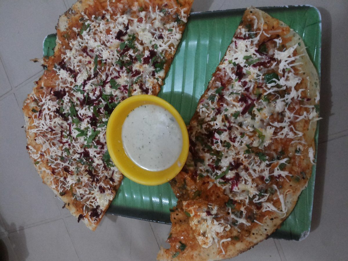 A cheese dosa cut in two on a banana leaf, with coconut chutney