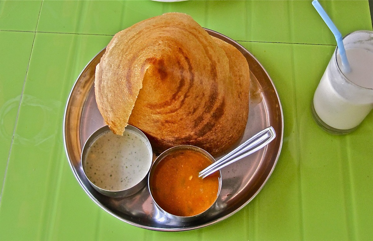 A paper-thin dosa curled on a steel plate with coconut chutney and sambar