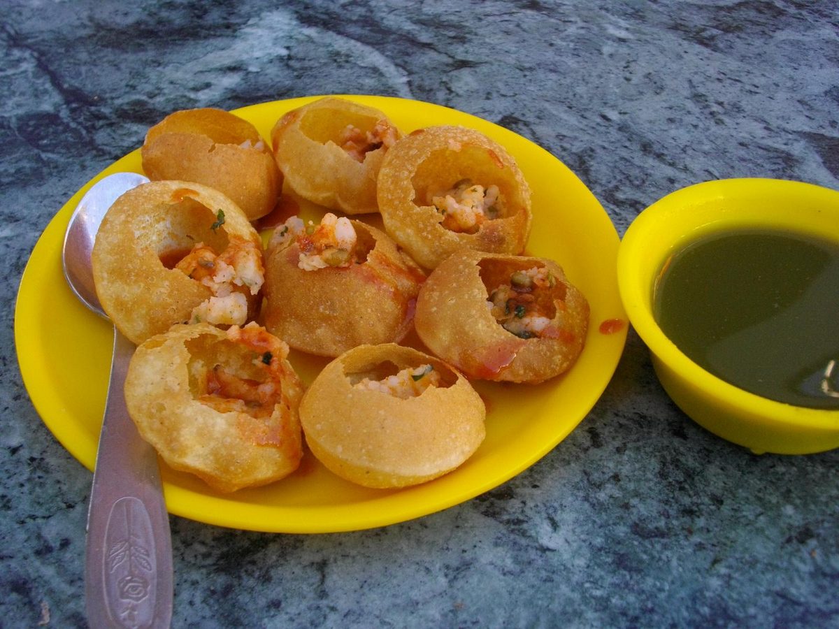 A plate of pani puri with a bowl of green pani